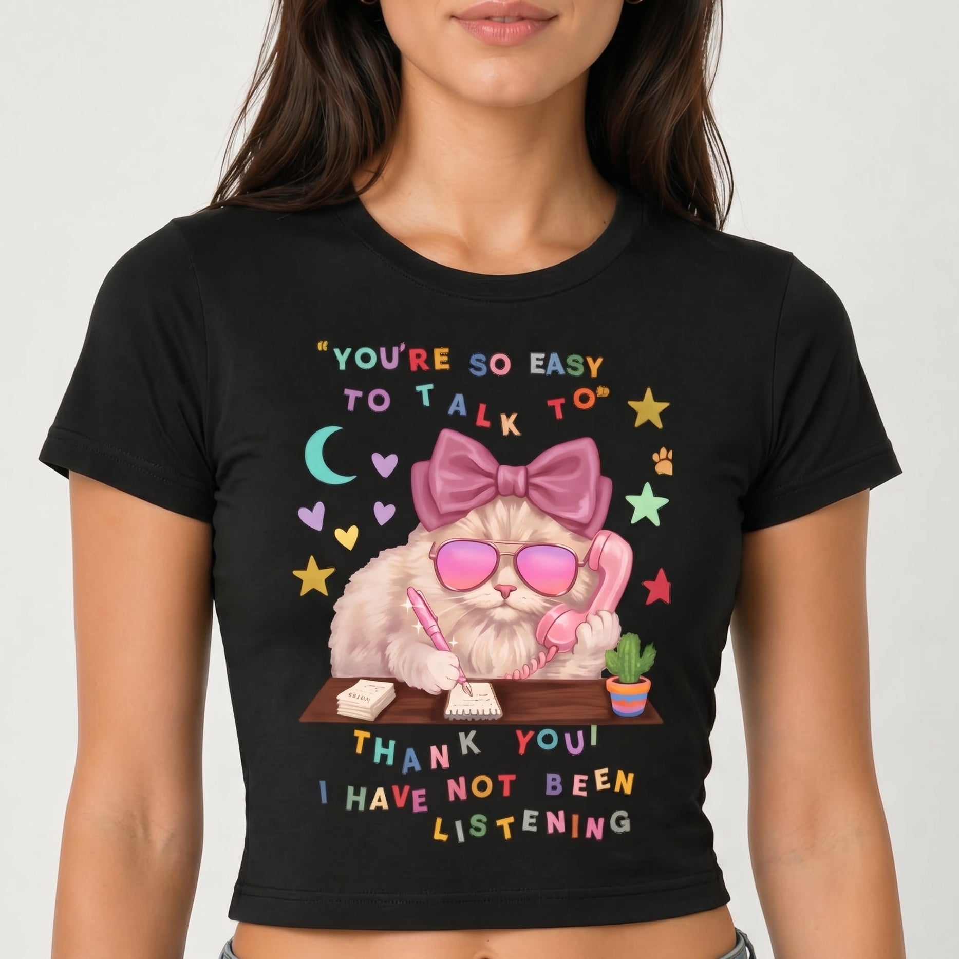 Black t-shirt with a graphic design of a cat wearing sunglasses and a bow, text, and a white background.